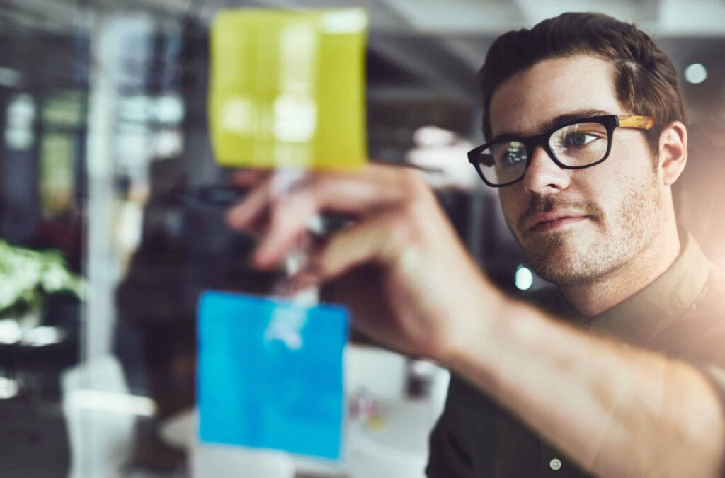 Designer placing sticky notes on a glass wall while mapping a product idea